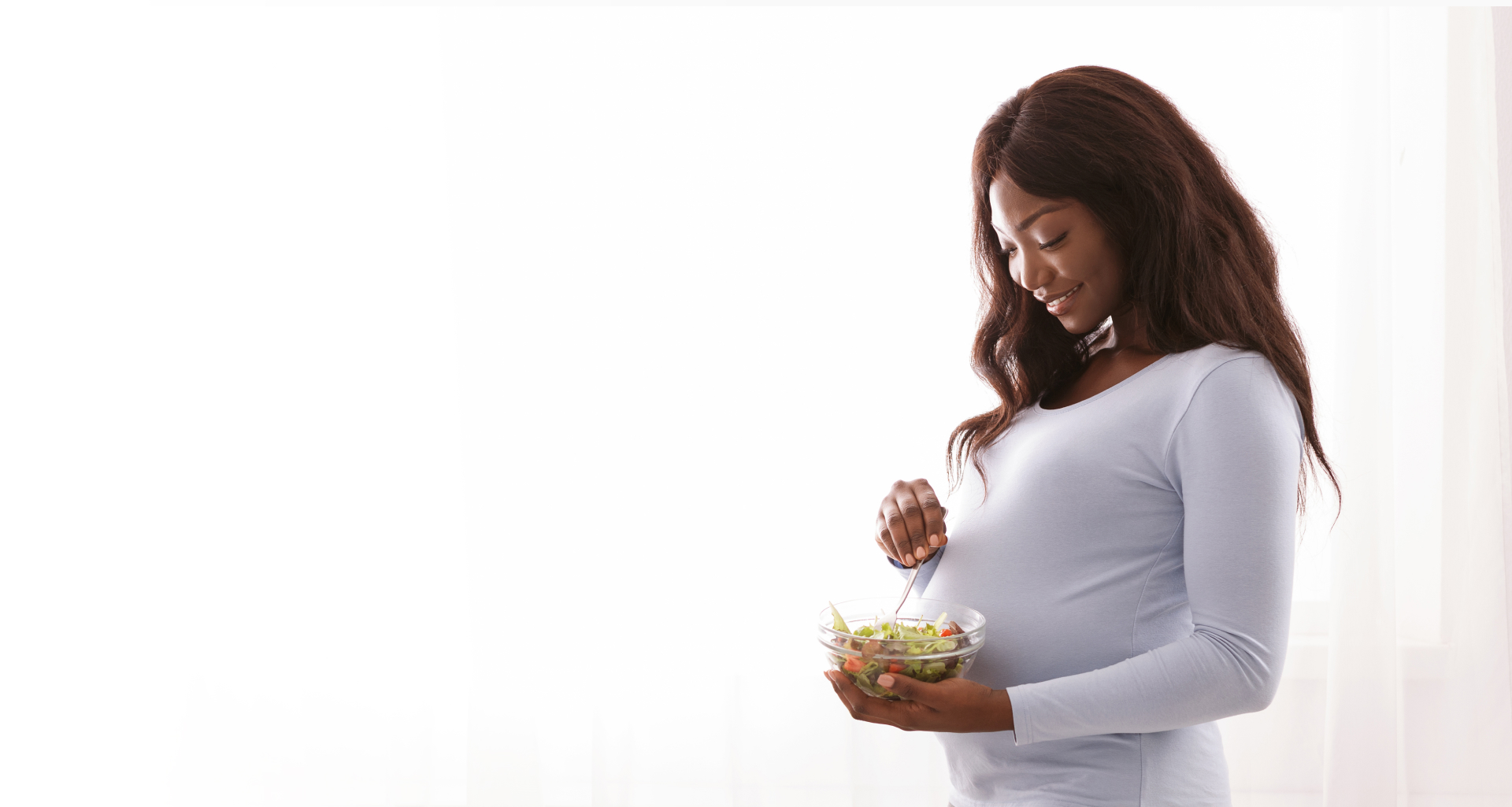 Pregnant woman eating fresh salad next to window at home